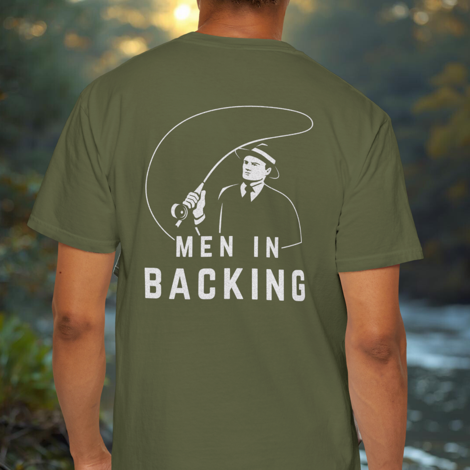 Model wearing olive/green tee showing the large “MEN IN BACKING” back print placement.