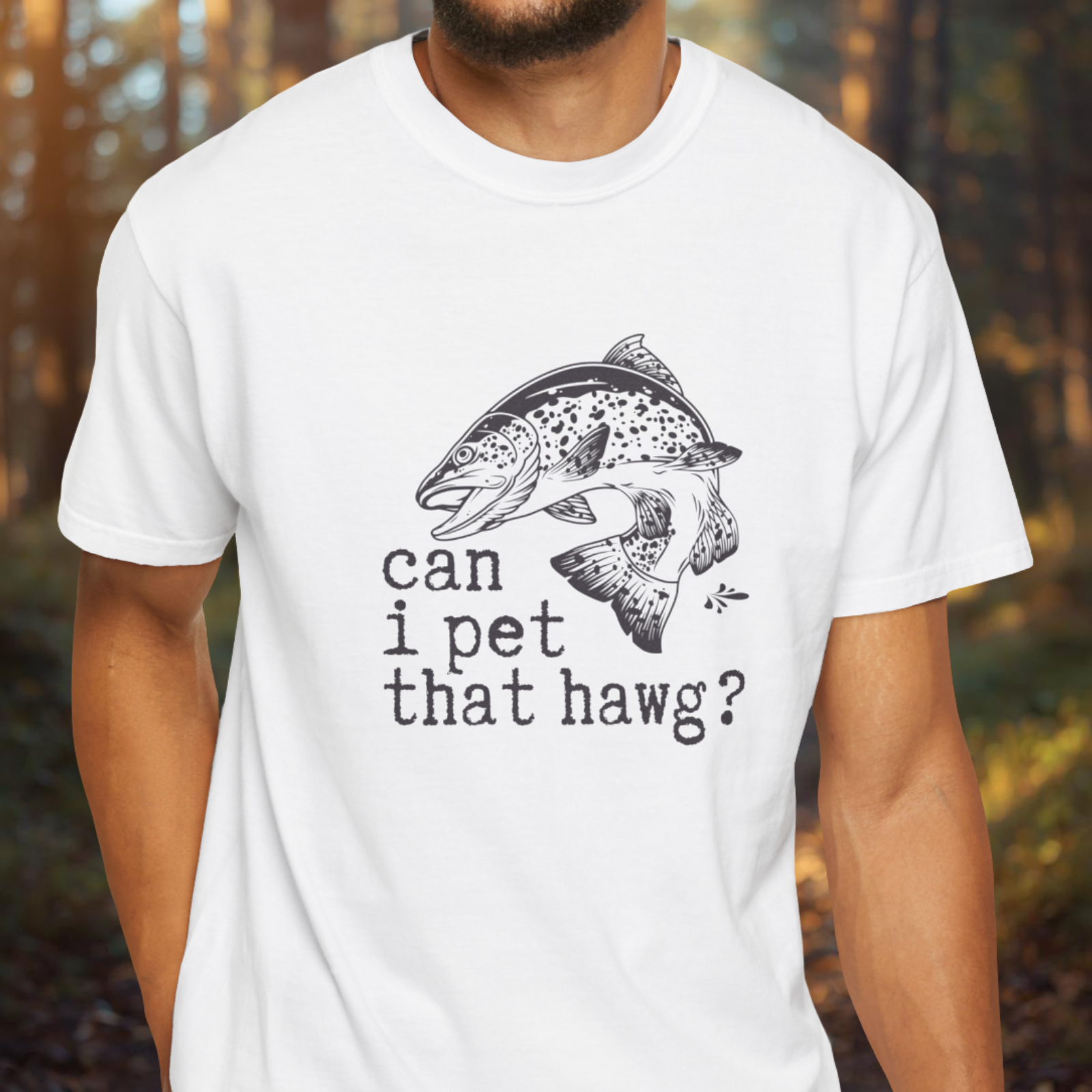 Person wearing a white t-shirt with a fish graphic and text in a forest setting
