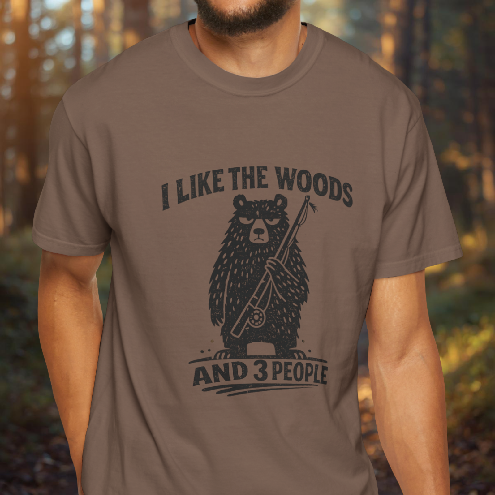 Person wearing a brown t-shirt with a bear graphic and text in a forest setting