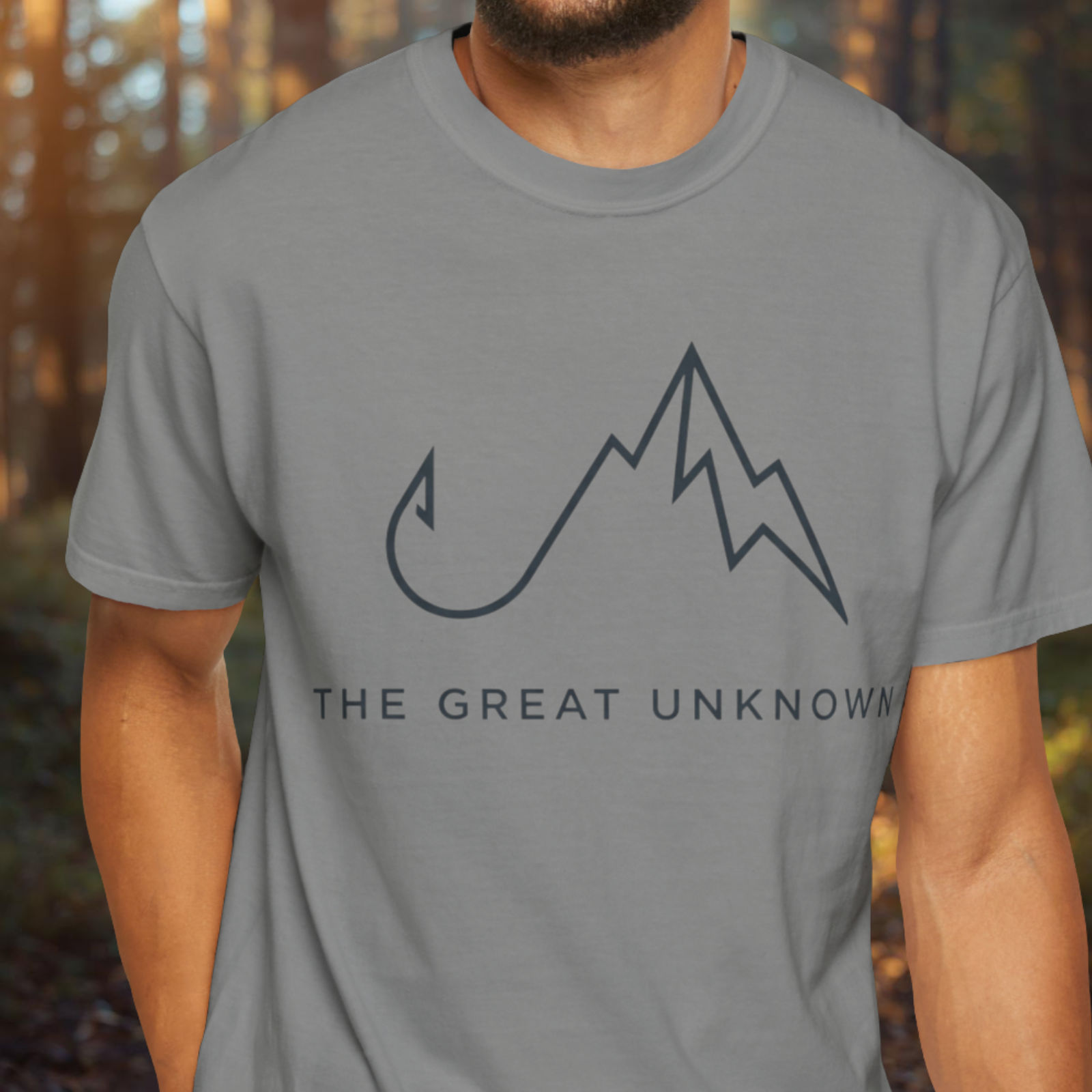 Person wearing a gray t-shirt with a mountain design and 'The Great Unknown' text in a forest setting.