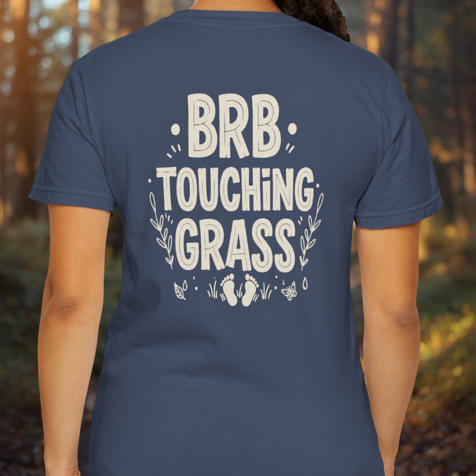 Person wearing a midnight t-shirt with 'BRB Touching Grass' text in a forest setting