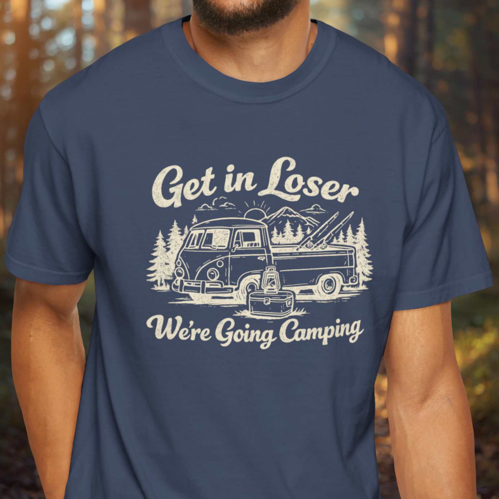 Navy blue t-shirt with a white graphic and text 'Get in Loser, We're Going Camping' worn by a person in a forest setting.