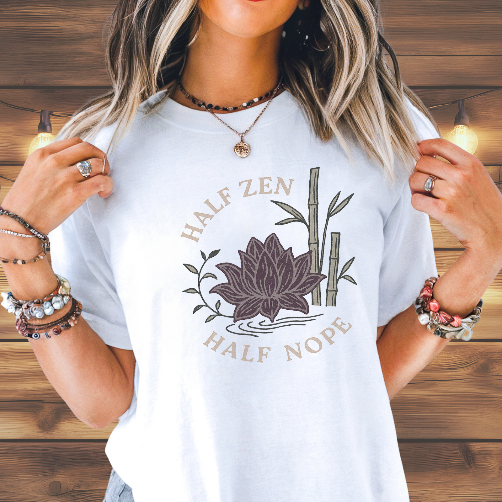 Woman Wearing a blush pink  t-shirt with hand-drawn lotus sunburst and “Half Zen Half Nope” text on a wood background