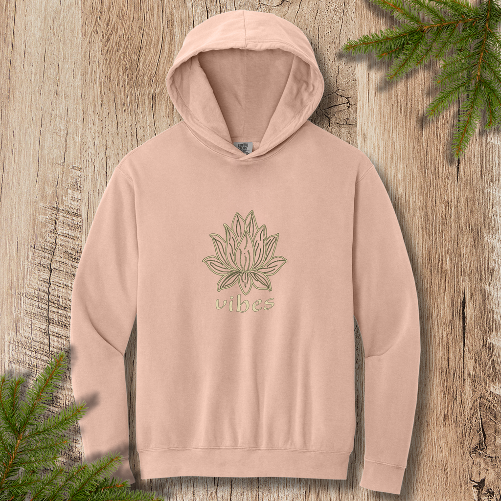 Peachy hoodie with line-drawn lotus flower and “vibes” text on a wooden background