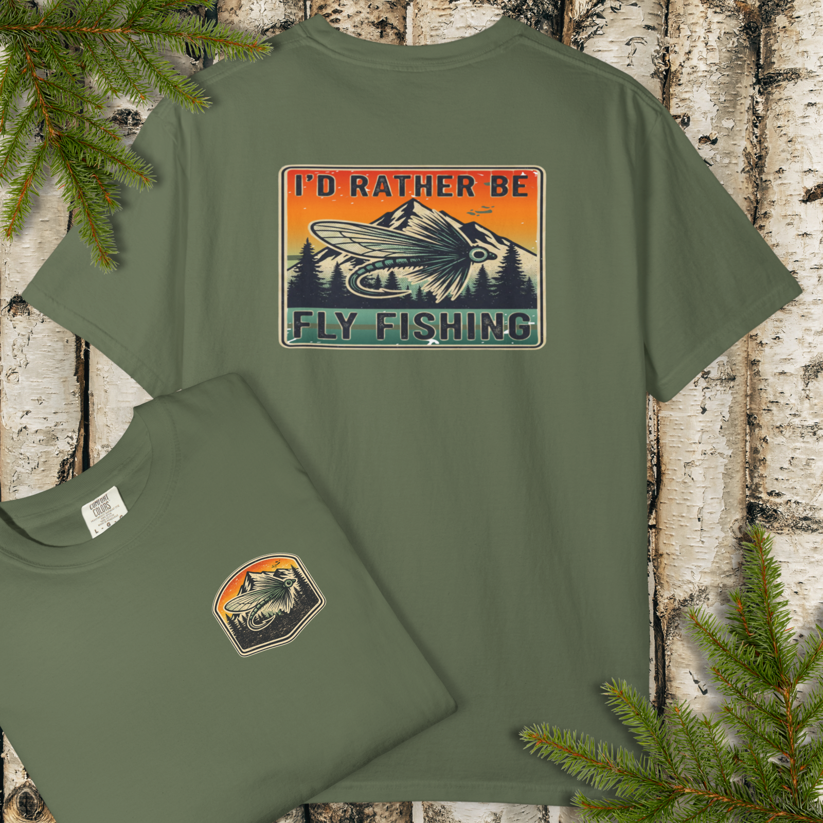Flat lay of green garment-dyed t-shirt with “I’d Rather Be Fly Fishing” retro sunset badge graphic (back print) and small front chest badge.