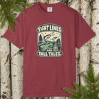 Maroon t-shirt with 'Tight Lines and Tall Tales' graphic design on a wooden background with pine branches.