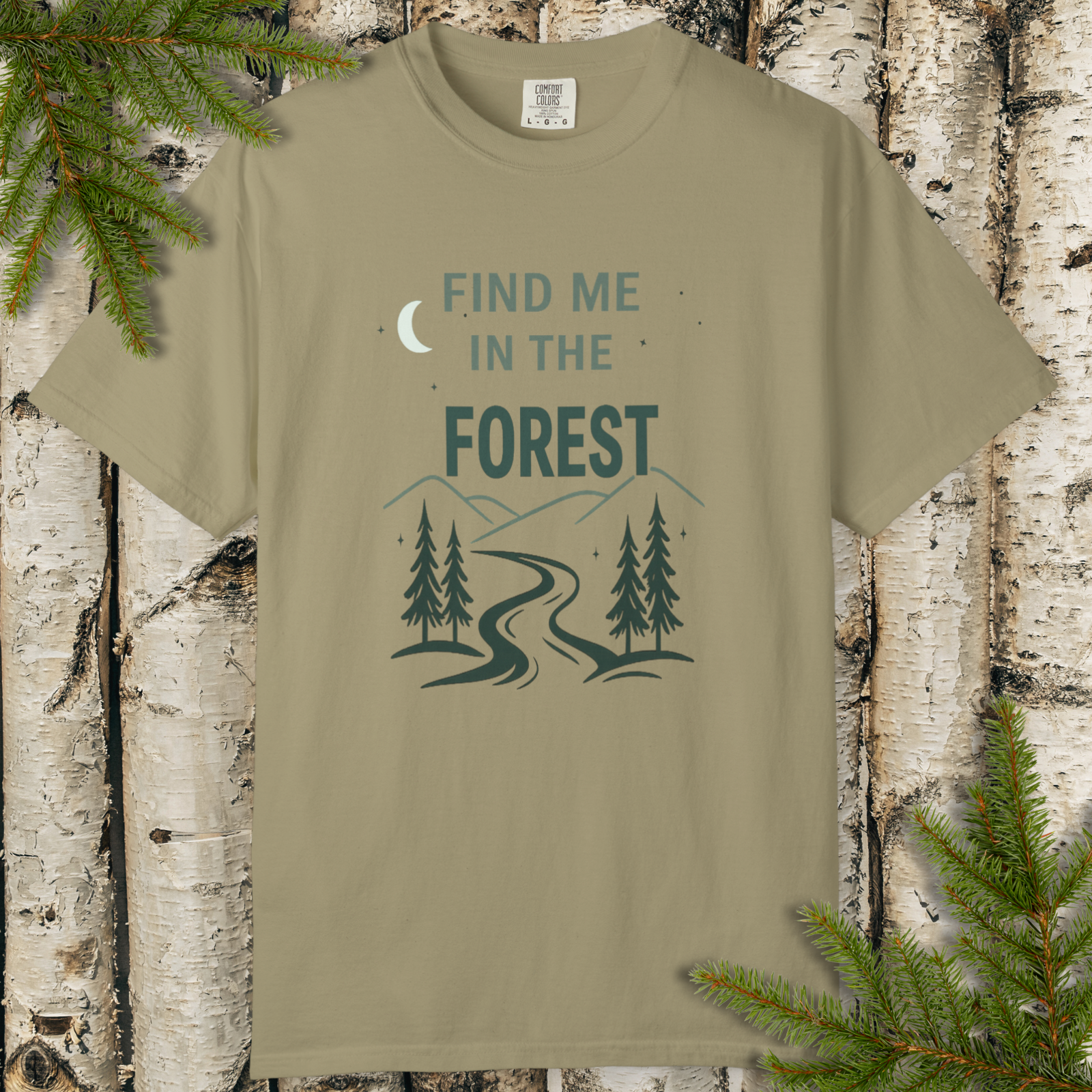 Khaki t-shirt with 'Find Me in the Forest' design on a wooden background with pine branches.