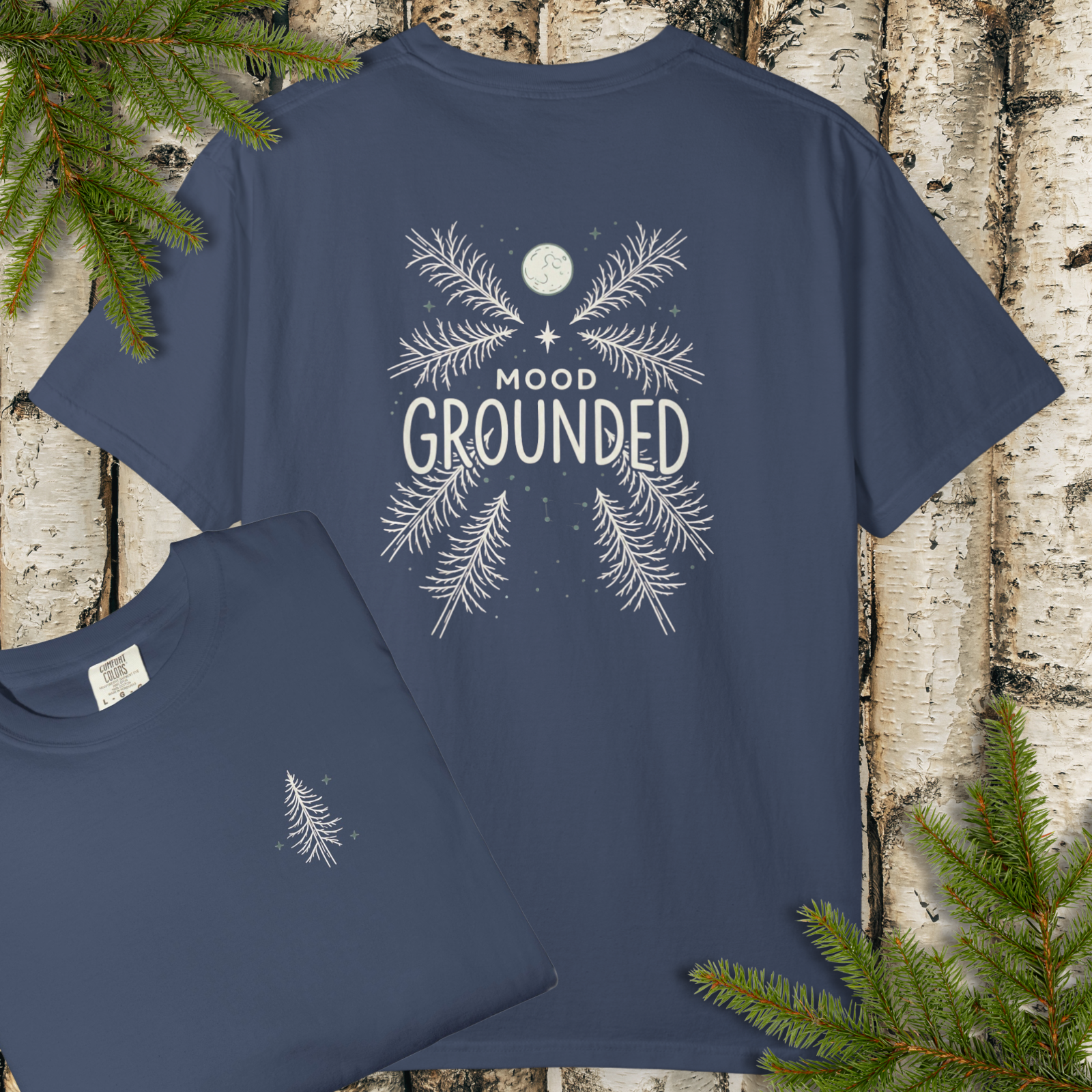 Navy blue t-shirt with 'Mood Grounded' design on a wooden surface with pine branches.
