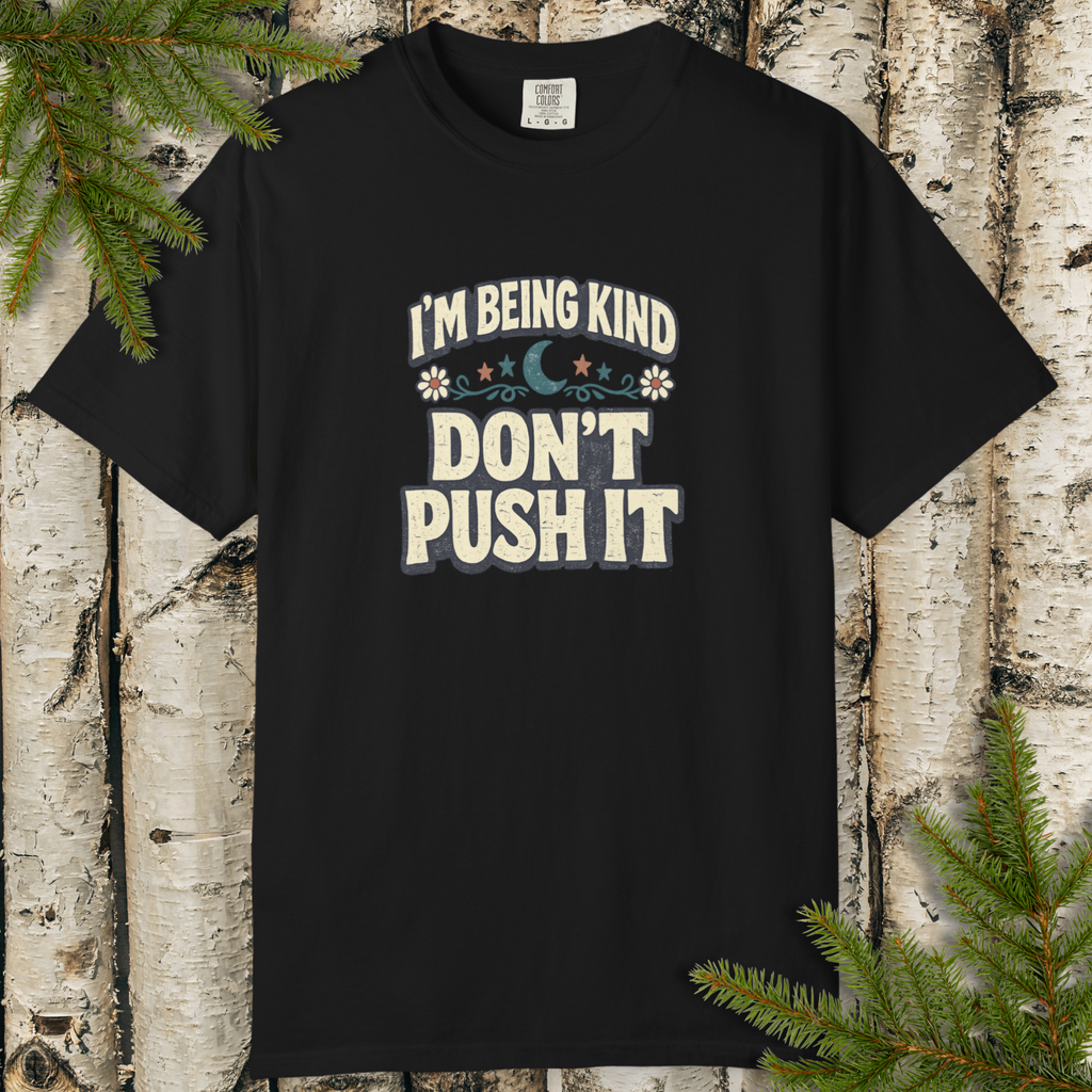 Black t-shirt with 'I'm being kind, don't push it' text on a wooden background with greenery.