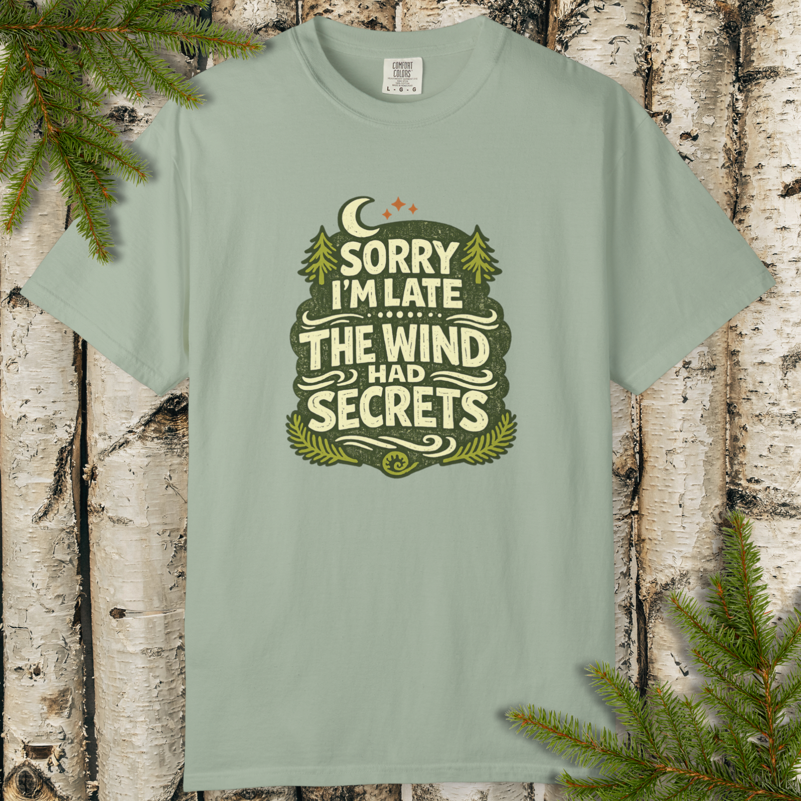 Bay green t-shirt with “Sorry I’m Late The Wind Had Secrets” forest patch graphic and crescent moon.