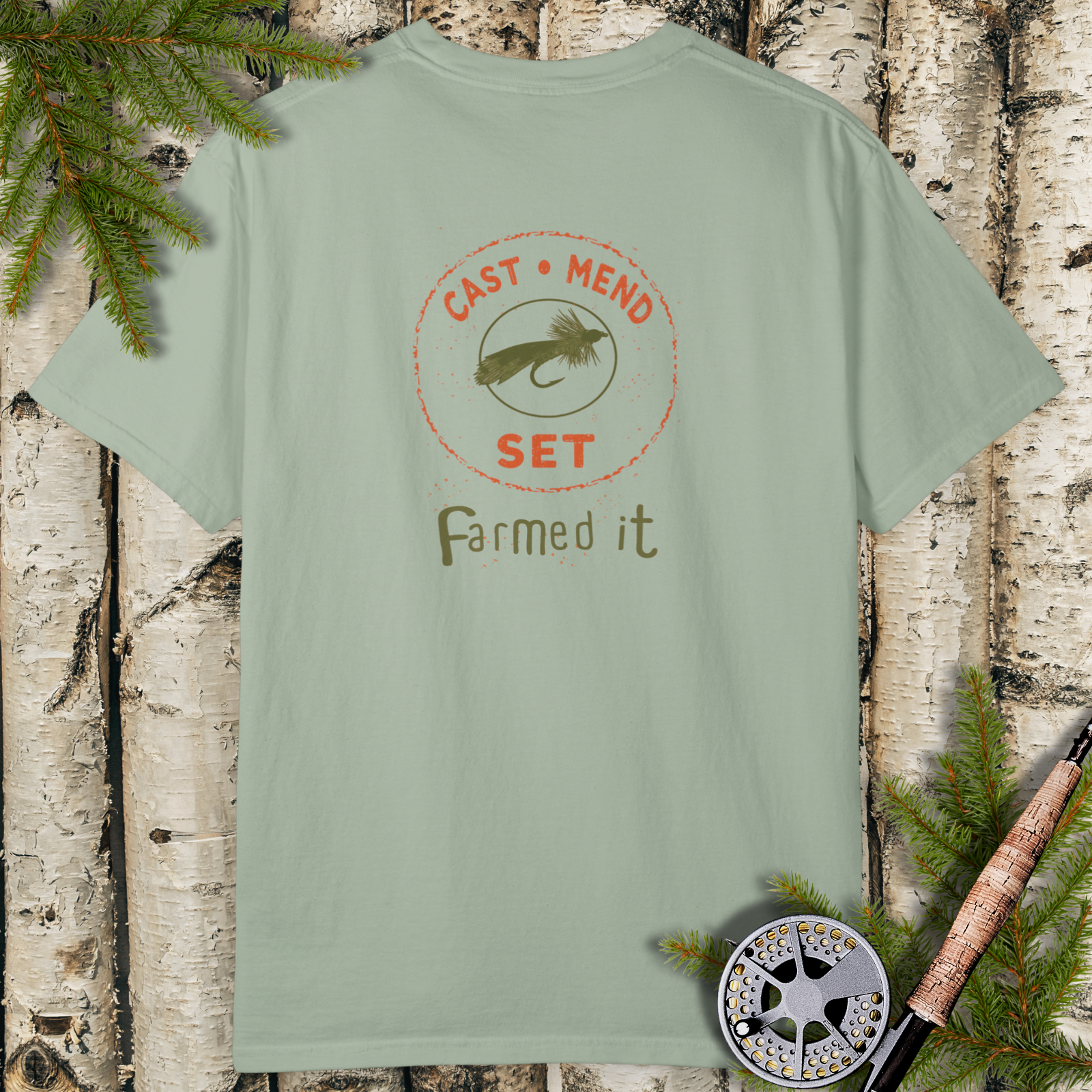 Bay green garment-dyed t-shirt with vintage “Cast • Mend • Set — Farmed it” fly fishing badge graphic on the front.