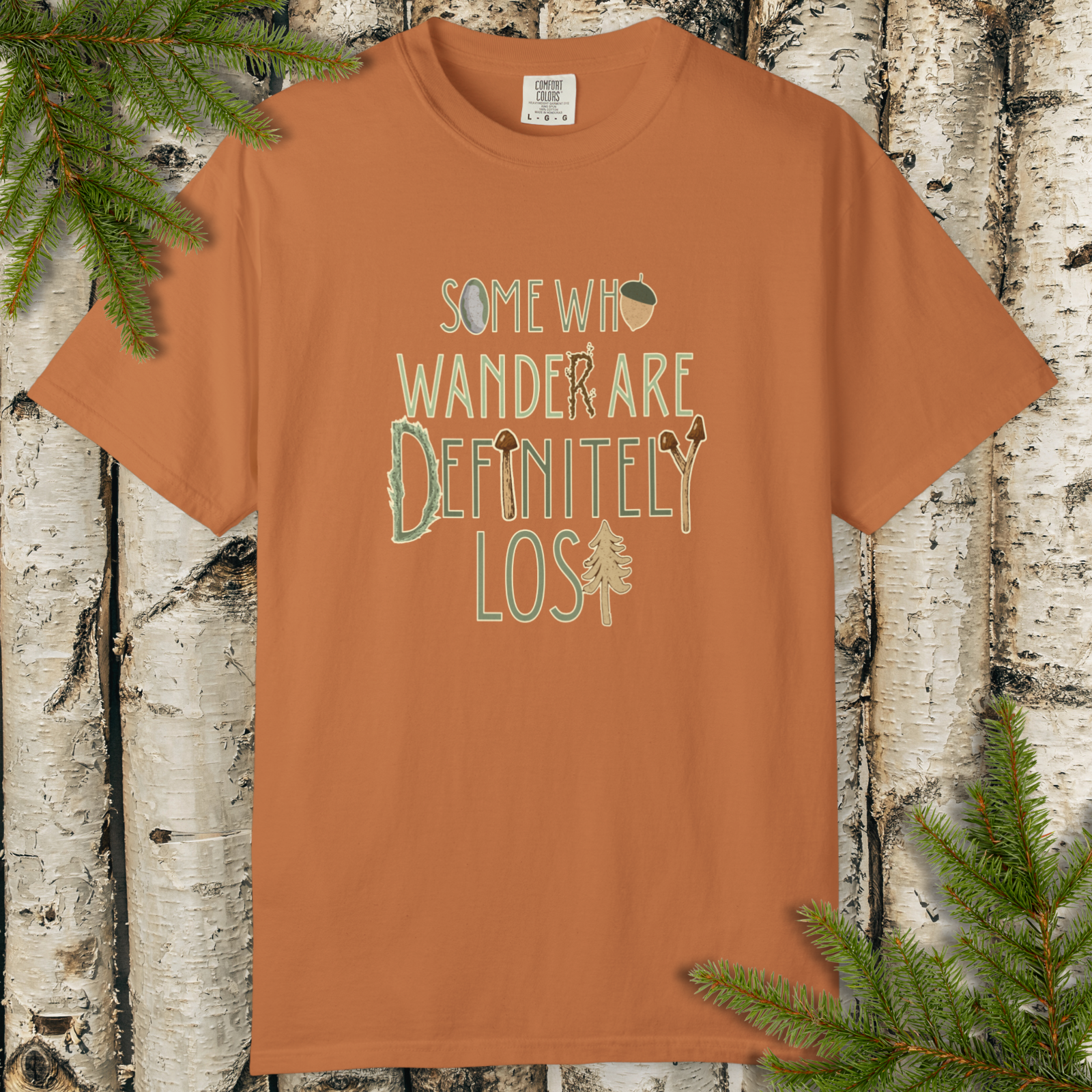 Brown/rust garment-dyed t-shirt with “Some Who Wander Are Definitely Lost” hand-lettered graphic on the front.