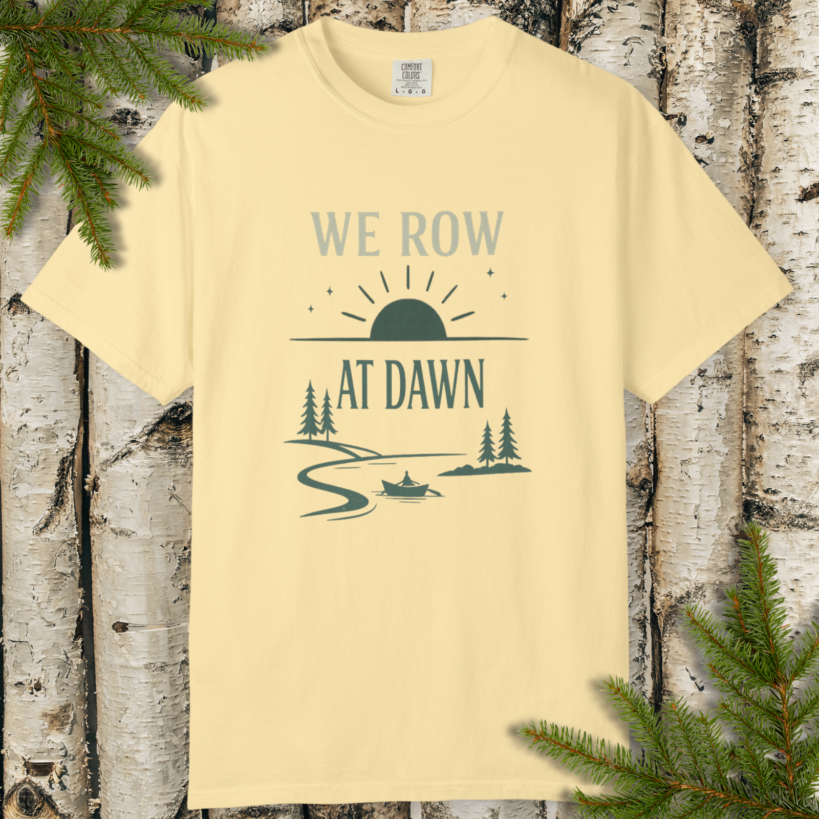 Yellow t-shirt with 'We Row at Dawn' graphic design on a wooden background with tree branches.