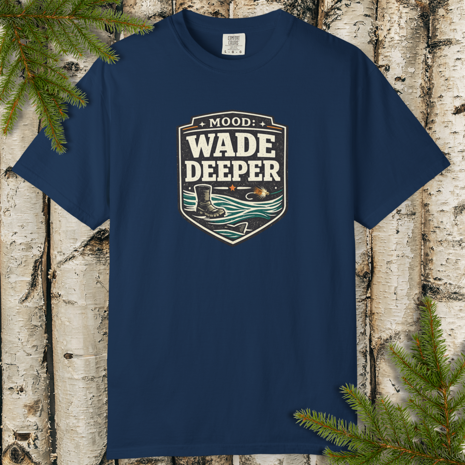 Navy blue t-shirt with 'Wade Deeper' graphic design on a wooden background with pine branches.