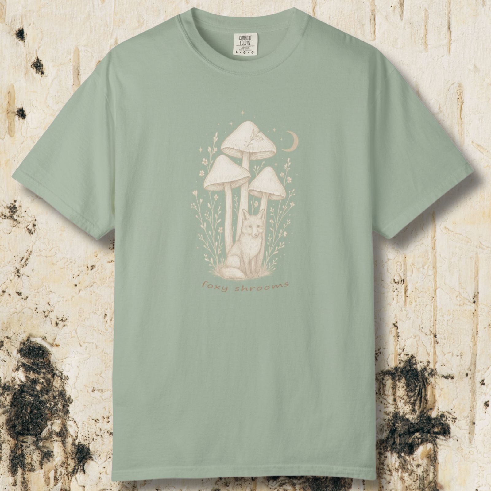 Sage green t-shirt with a fox and mushroom design on a textured beige background
