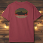Back view of garment-dyed unisex t-shirt with circular brown trout illustration on wooden backdrop.