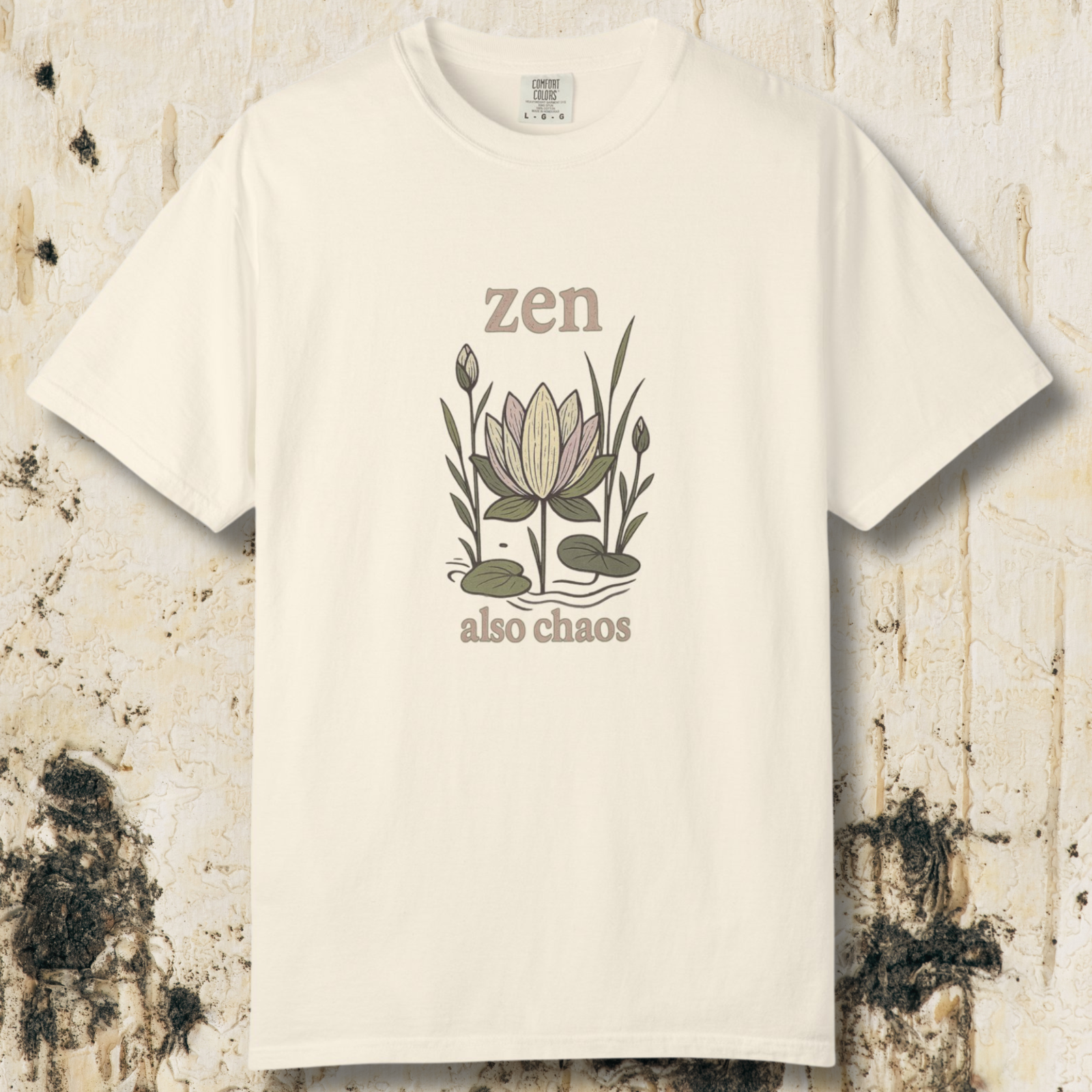 Ivory t-shirt with hand-drawn lotus illustration and “zen also chaos” text on a textured neutral background