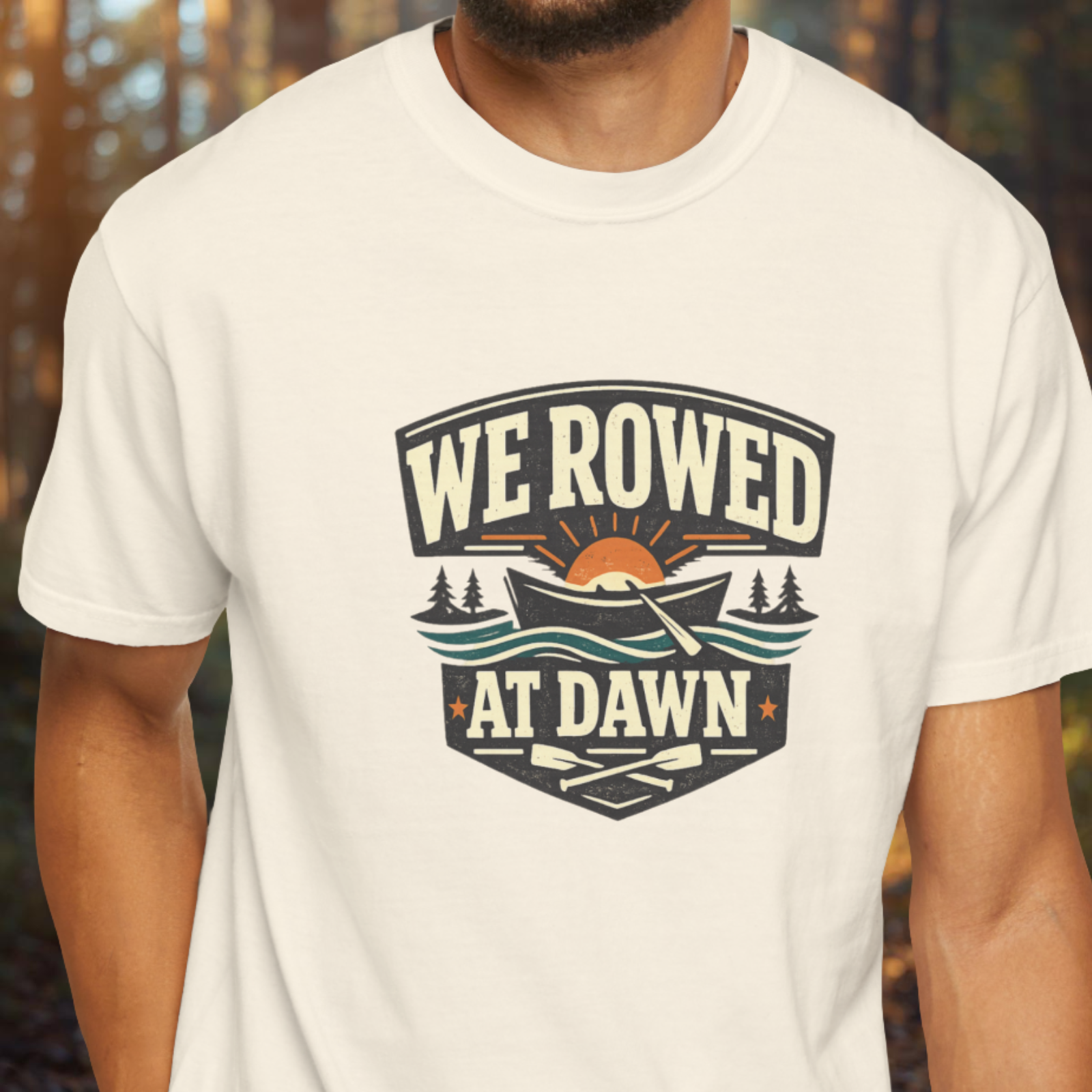 White t-shirt with 'We Rowed at Dawn' graphic design on a blurred natural background