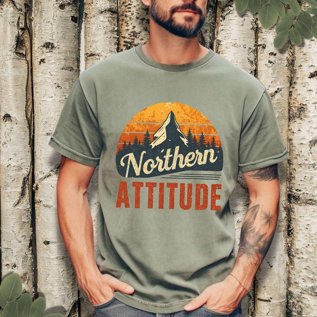 Person wearing a terracotta “Northern Attitude” mountain sunset graphic tee in a casual outdoor setting.