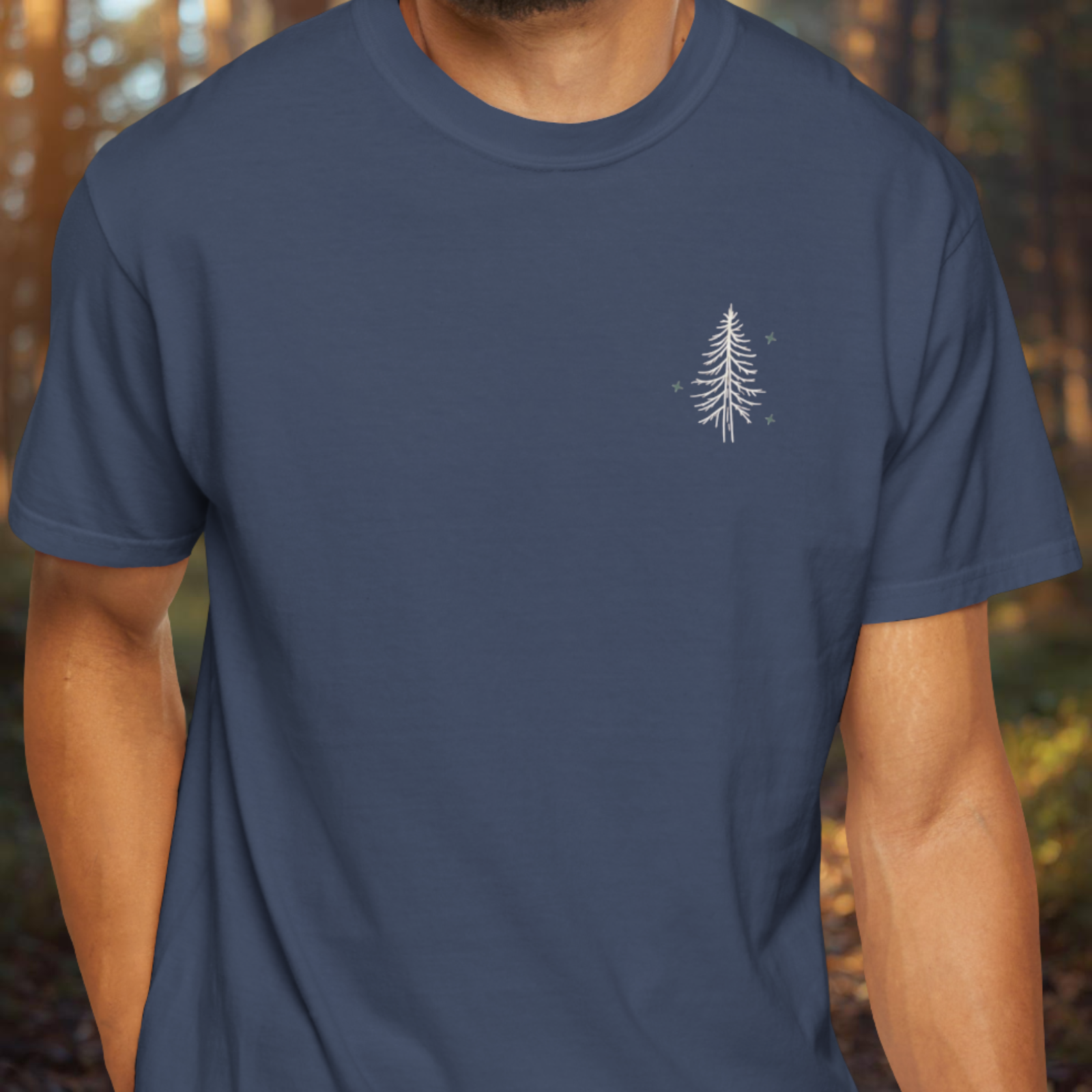 Person wearing a navy blue t-shirt with a white tree design in a forest setting