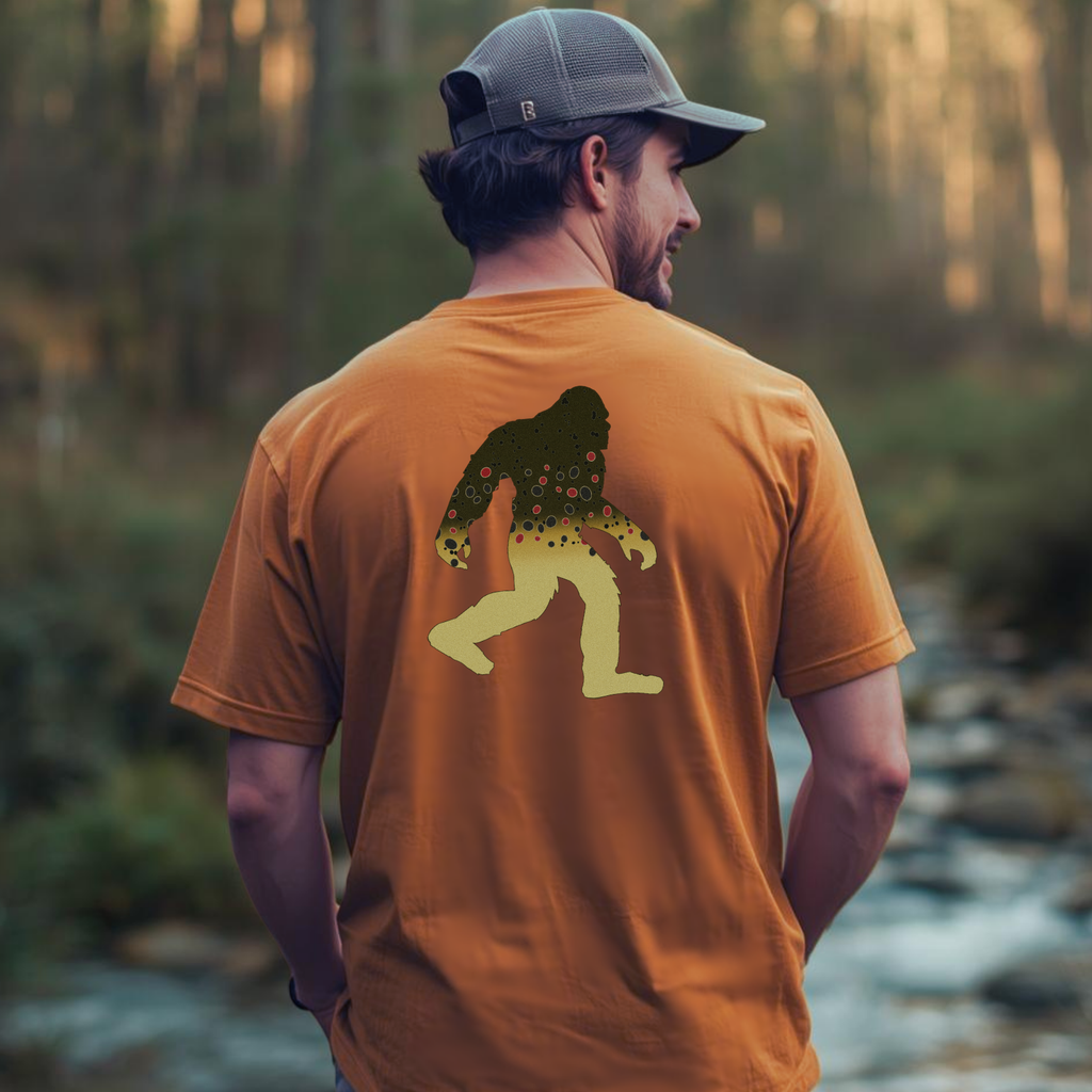 Person wearing Squatch Brownie brown trout Bigfoot tee outdoors