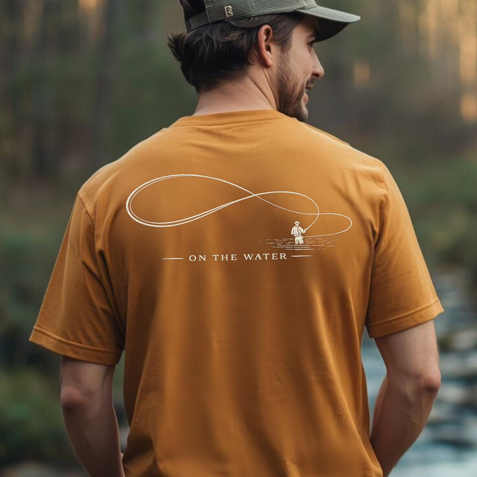 Man wearing a mustard yellow t-shirt with 'On the Water' design, standing by a body of water.
