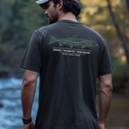 Person wearing a brown trout topography graphic t-shirt outdoors near the water.