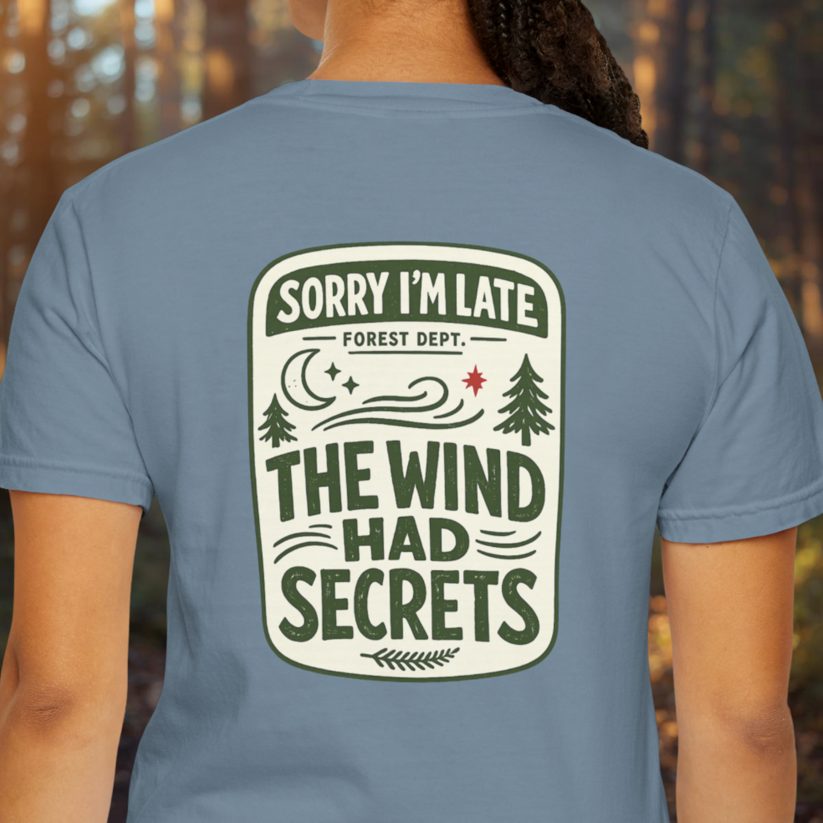 Model wearing ‘Sorry I’m Late The Wind Had Secrets’ graphic tee with forest sign style print on back.