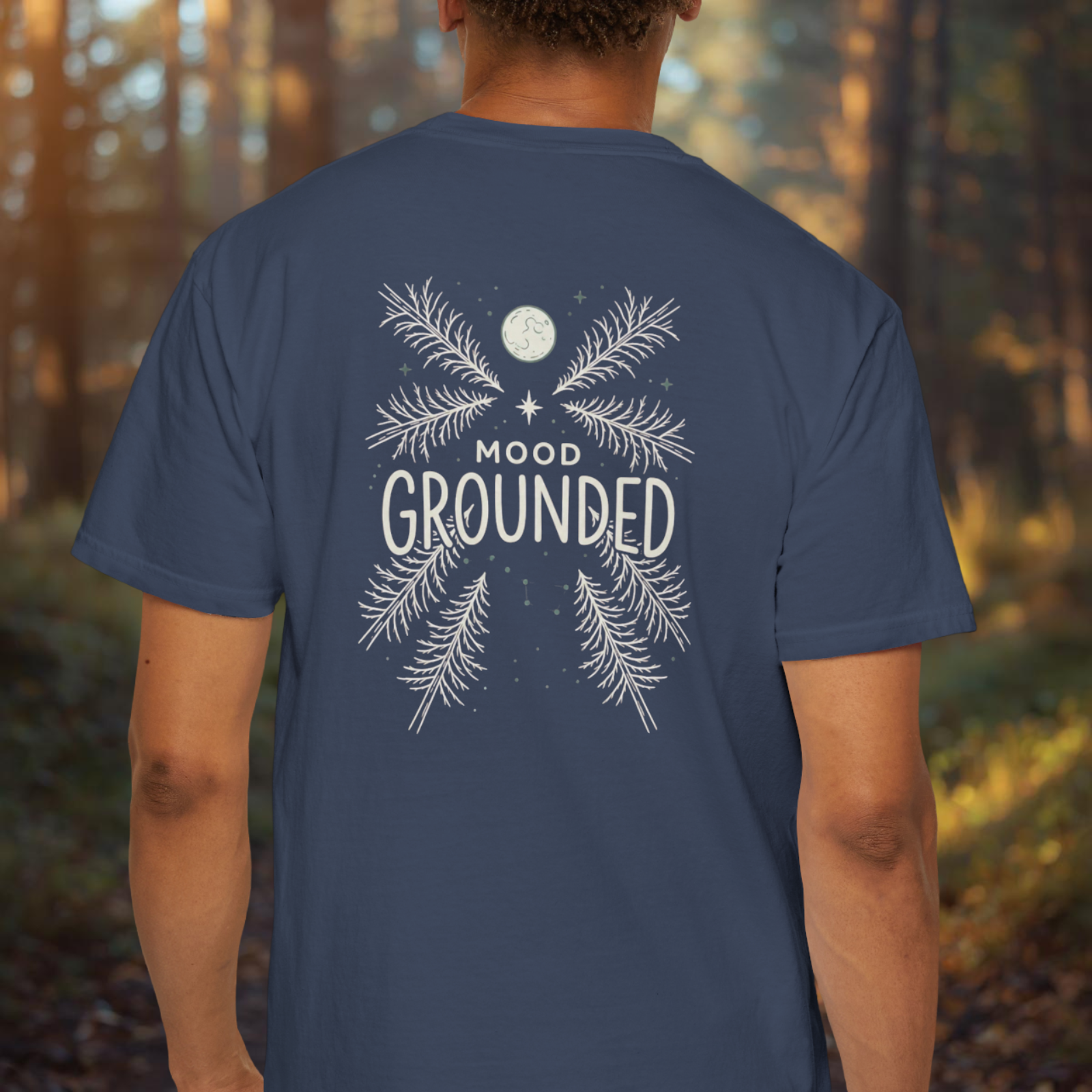 Person wearing a blue t-shirt with 'Mood Grounded' design in a forest setting