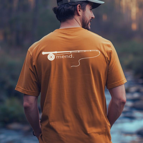 Fly fisher wearing ‘Mend.’ fishing rod graphic t-shirt near water