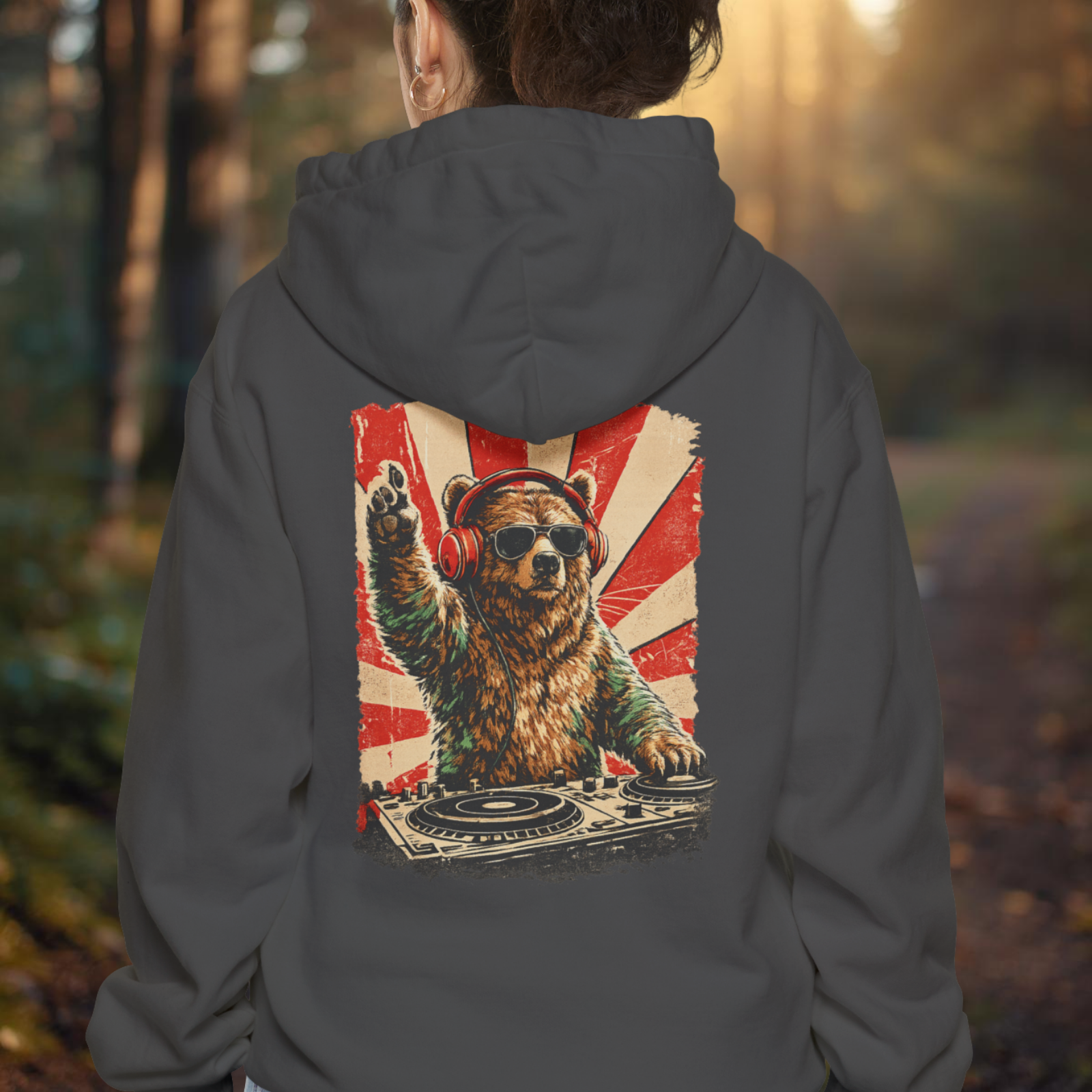 Person wearing a hoodie with a bear DJ design on the back in a forest setting