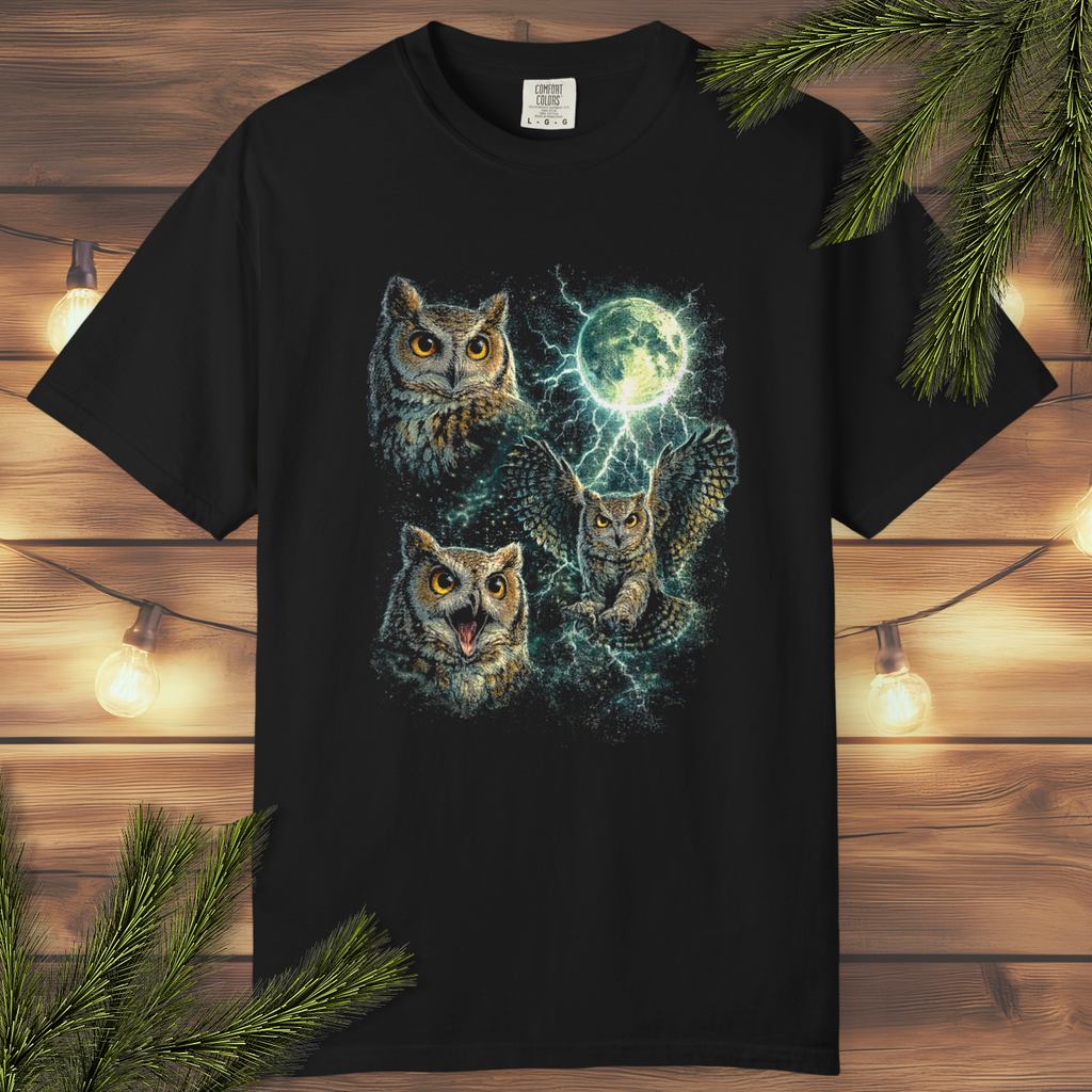 Black t-shirt with owl design on a wooden surface with lights and branches.