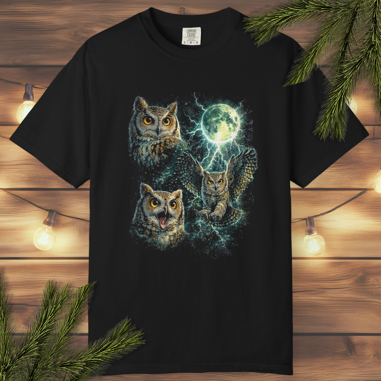 Black t-shirt with owl design on a wooden surface with lights and branches.