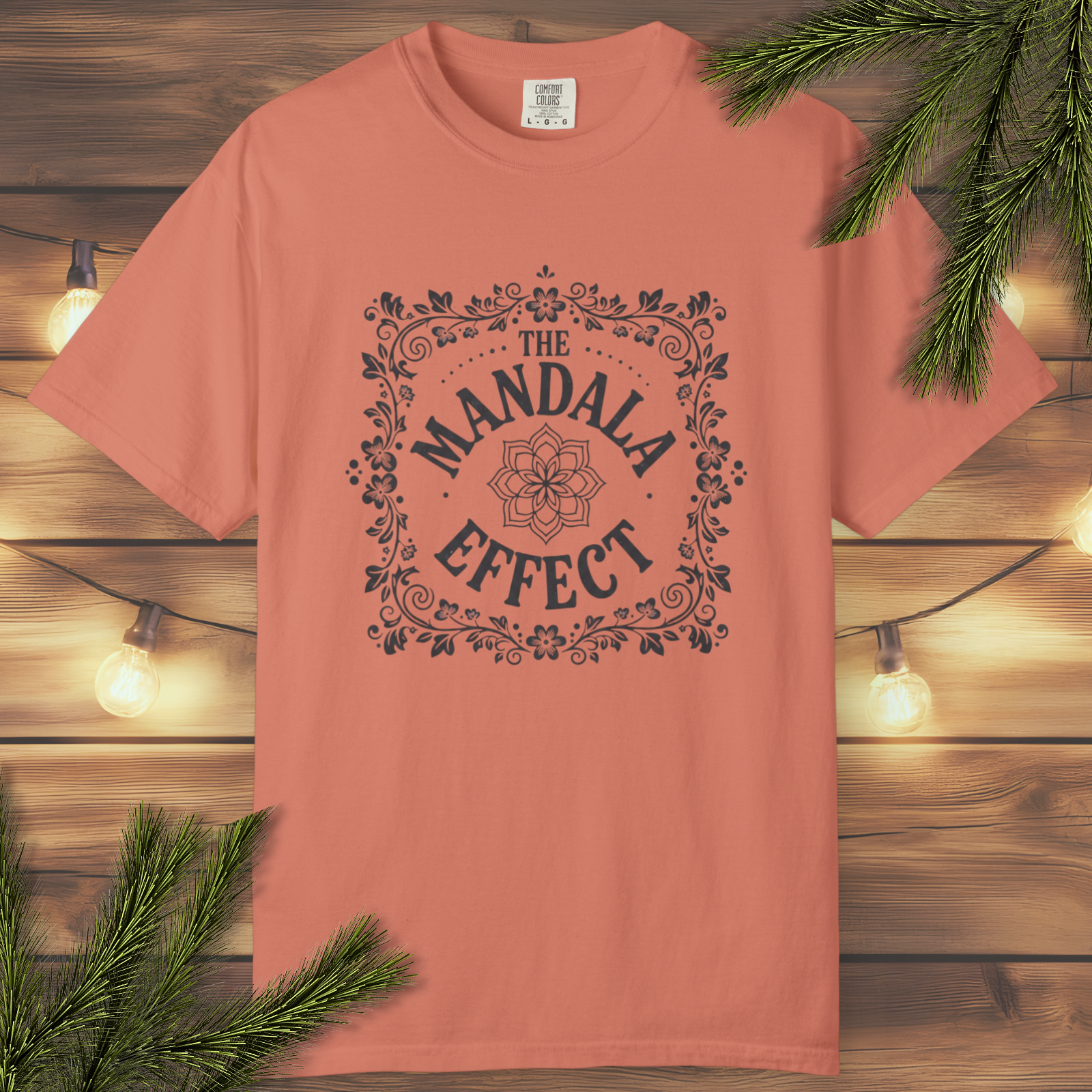 Terracotta t-shirt with 'The Mandala Effect' design on a wooden background with lights and greenery.