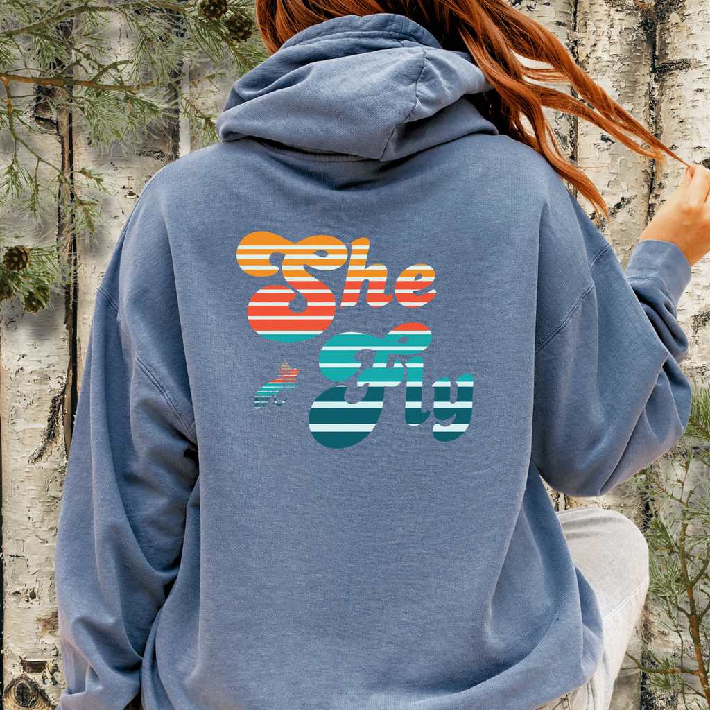 Back view of blue jean hoodie with large “She Fly” retro striped graphic inspired by women who fly fish.