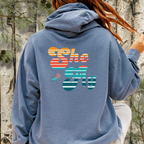 Back view of blue jean hoodie with large “She Fly” retro striped graphic inspired by women who fly fish.