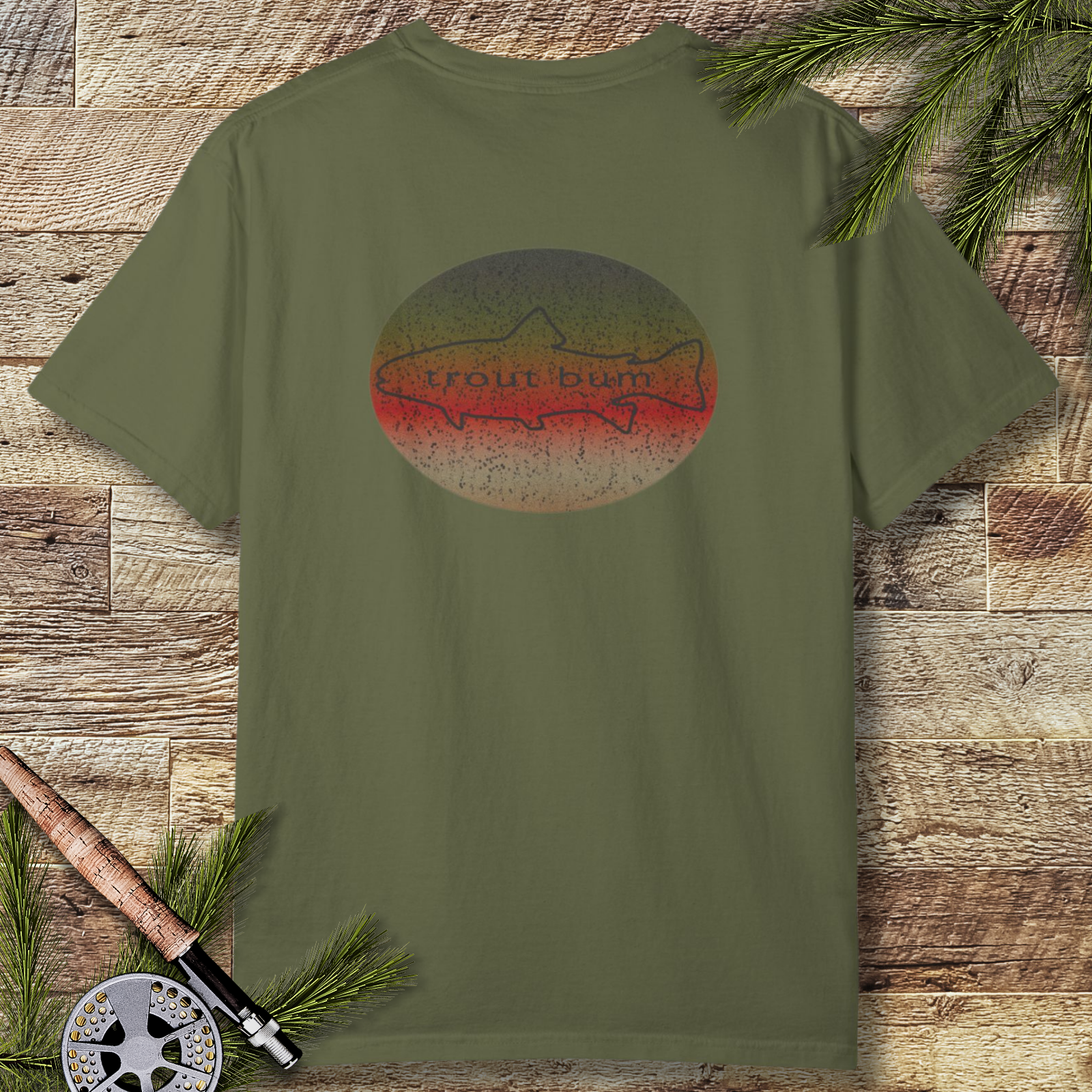 Hemp green t-shirt with retro “trout bum” rainbow trout illustration on the back, styled flat on rustic wood with fly-fishing rod and evergreen branches