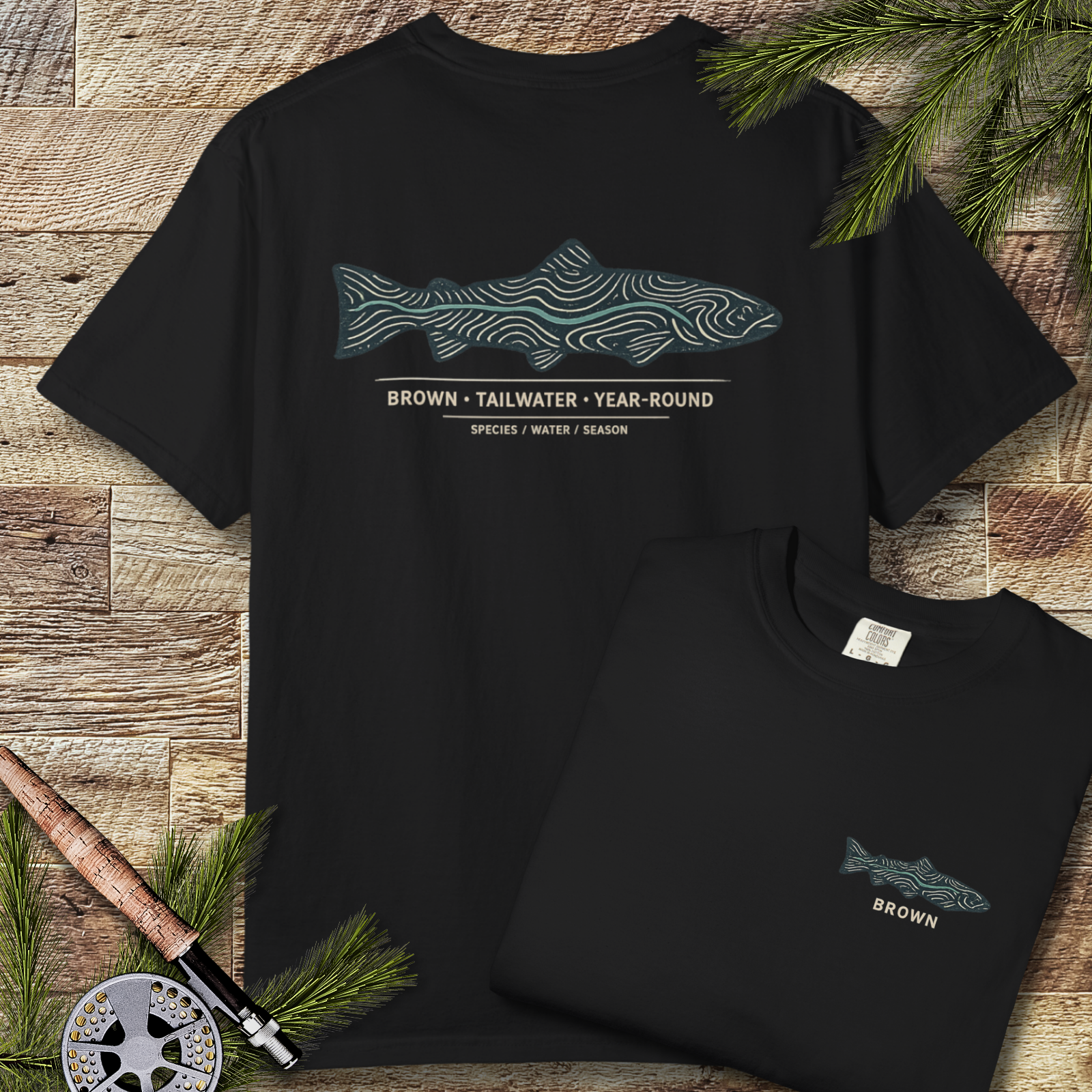 Black garment-dyed t-shirt with brown trout topography graphic on the back, laid flat on a rustic wood background.