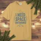 Mustard t-shirt with 'I Need Space Outdoors' text on a wooden background with greenery.