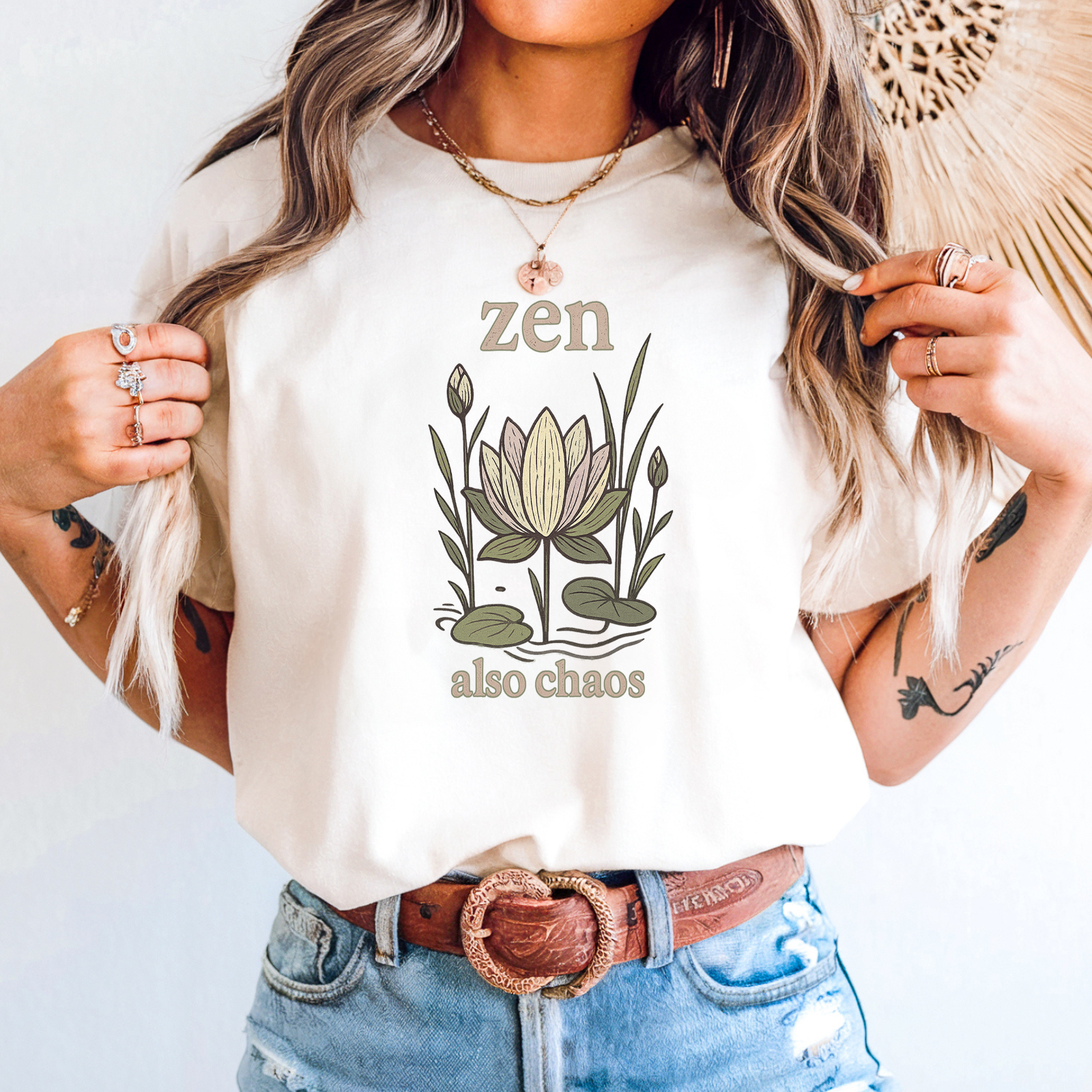 Woman wearing ivory “zen also chaos” lotus graphic t-shirt styled with denim shorts and jewelry