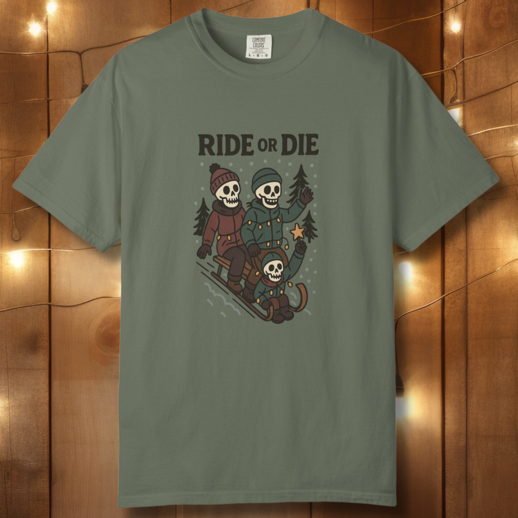 Moss green unisex t-shirt with “Ride or Die” skeleton sledding graphic on a wood backdrop with string lights